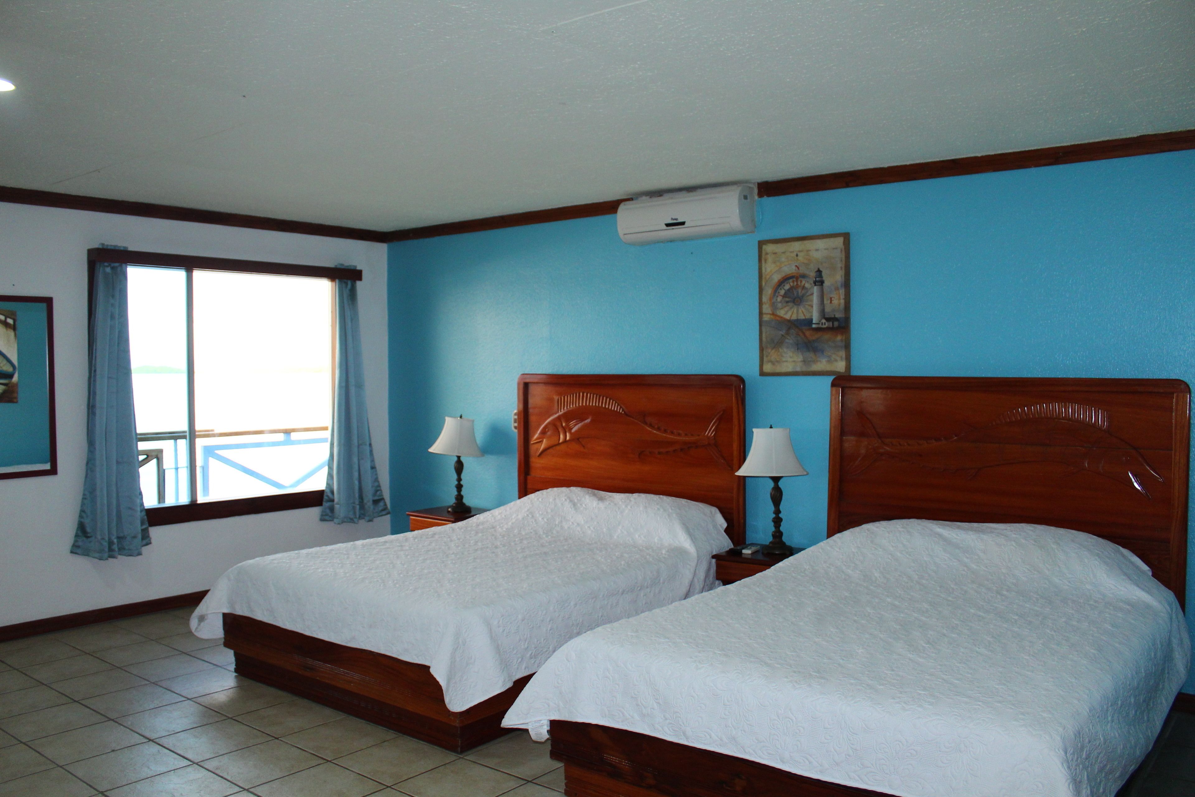 Habitació d'hotel amb dos llits de fusta, un gran finestral amb cortines i un quadre al mur.