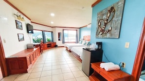 A spacious hotel room with a large bed, a desk, a TV, and a balcony with a view of boats. - Fish Hook Marina & Lodge (Golfito)