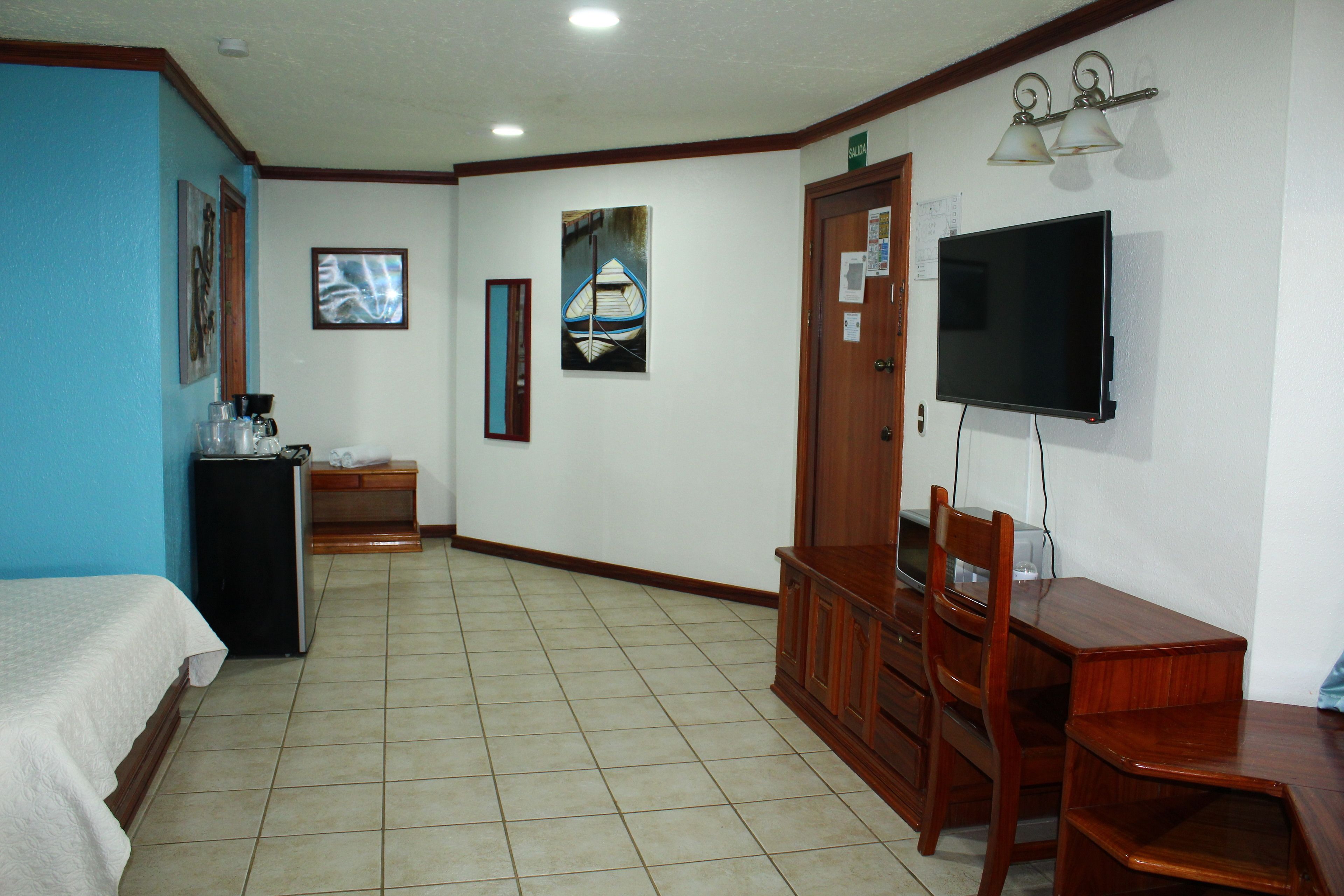 Una habitación de hotel con cama, escritorio, silla, televisor y una pequeña kitchenette.