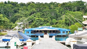 A marina with a blue building labeled "Fish Hook Marina & Lodge" at the dock. - Fish Hook Marina & Lodge (Golfito)
