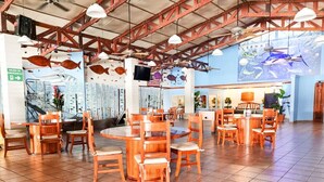 A spacious restaurant with wooden tables and chairs, a high ceiling with exposed beams, and a mural of fish on the wall. - Fish Hook Marina & Lodge (Golfito)