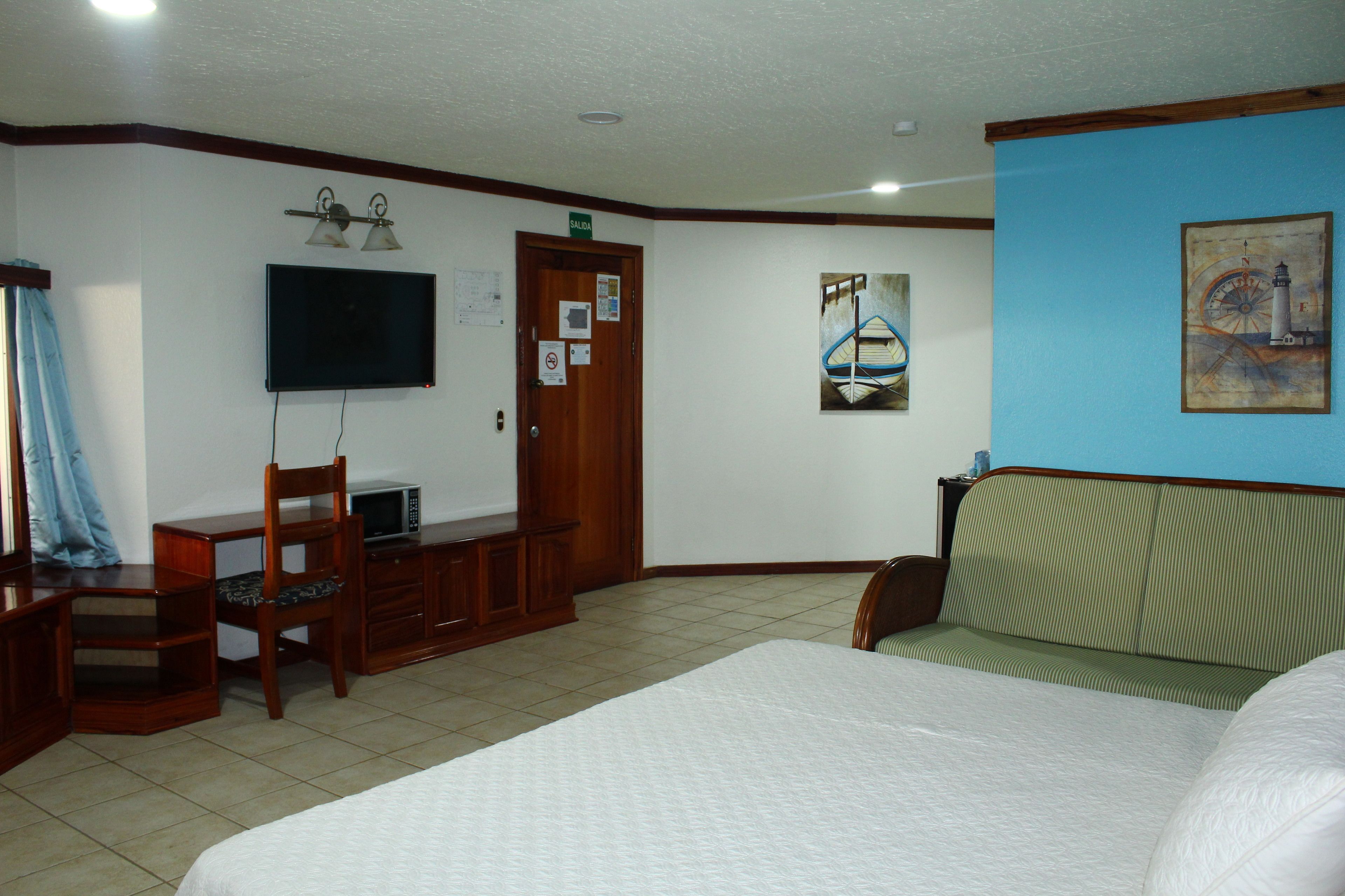 A hotel room with a bed, a desk with a chair, a television, and artwork on the walls.