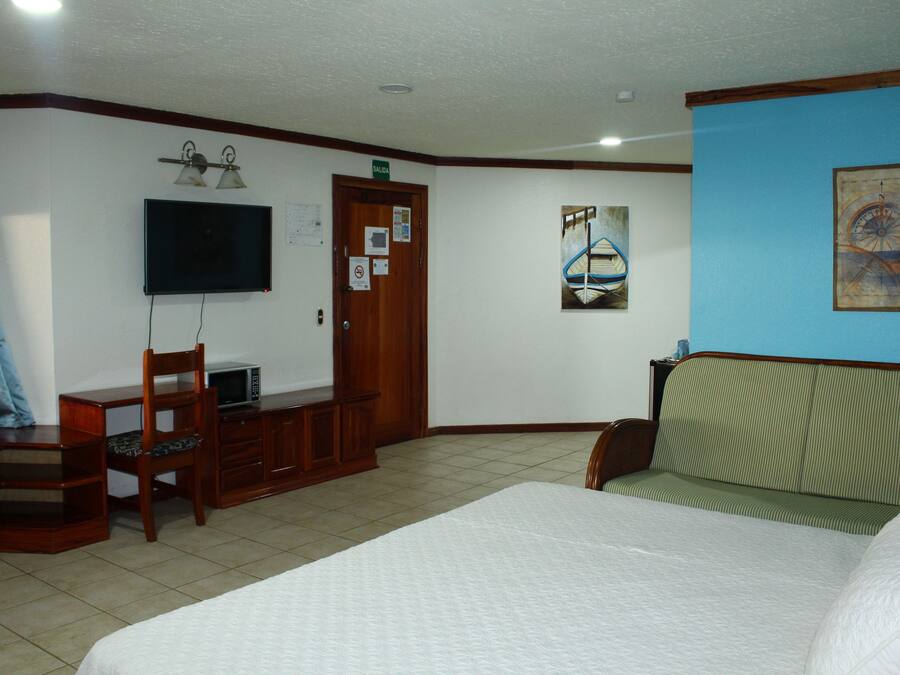Habitación de hotel con cama, escritorio con silla, televisión y obras de arte en las paredes.