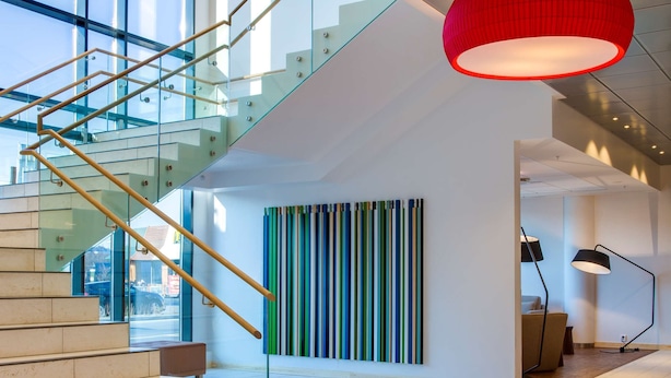 Un interior moderno con una escalera, una lámpara colgante roja y una obra de arte con motivos a rayas.