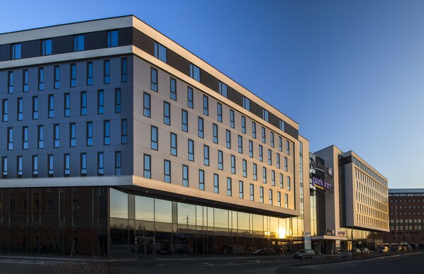 A modern hotel with a glass facade, multiple floors, and a parking lot in front. - Radisson Blu Hotel Oslo Alna (Oslo)