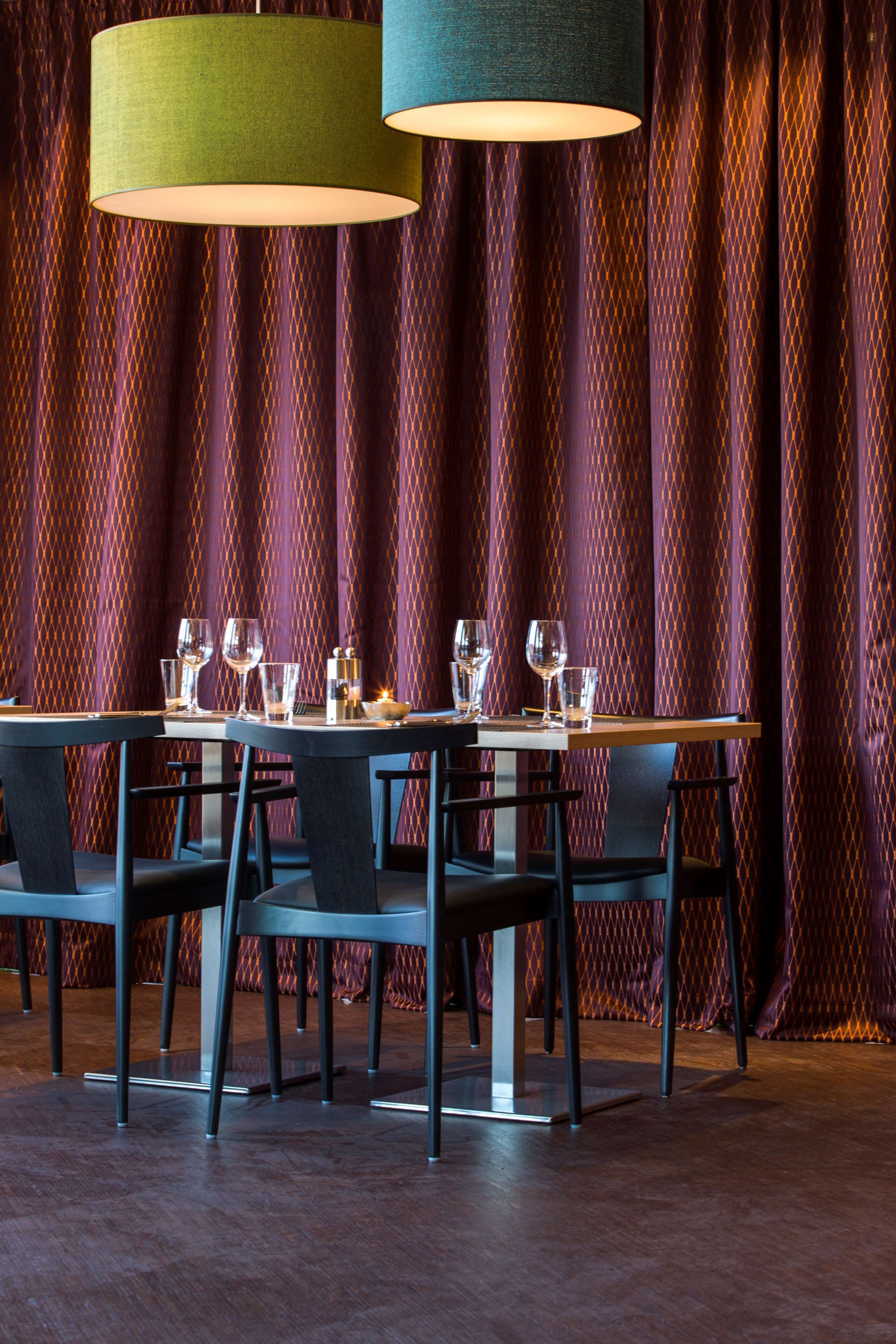 Comedor con una mesa preparada para cuatro personas, dos lámparas colgantes y un fondo de cortina estampada.