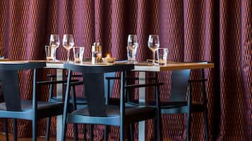 Comedor con una mesa preparada para cuatro personas, dos lámparas colgantes y un fondo de cortina estampada.