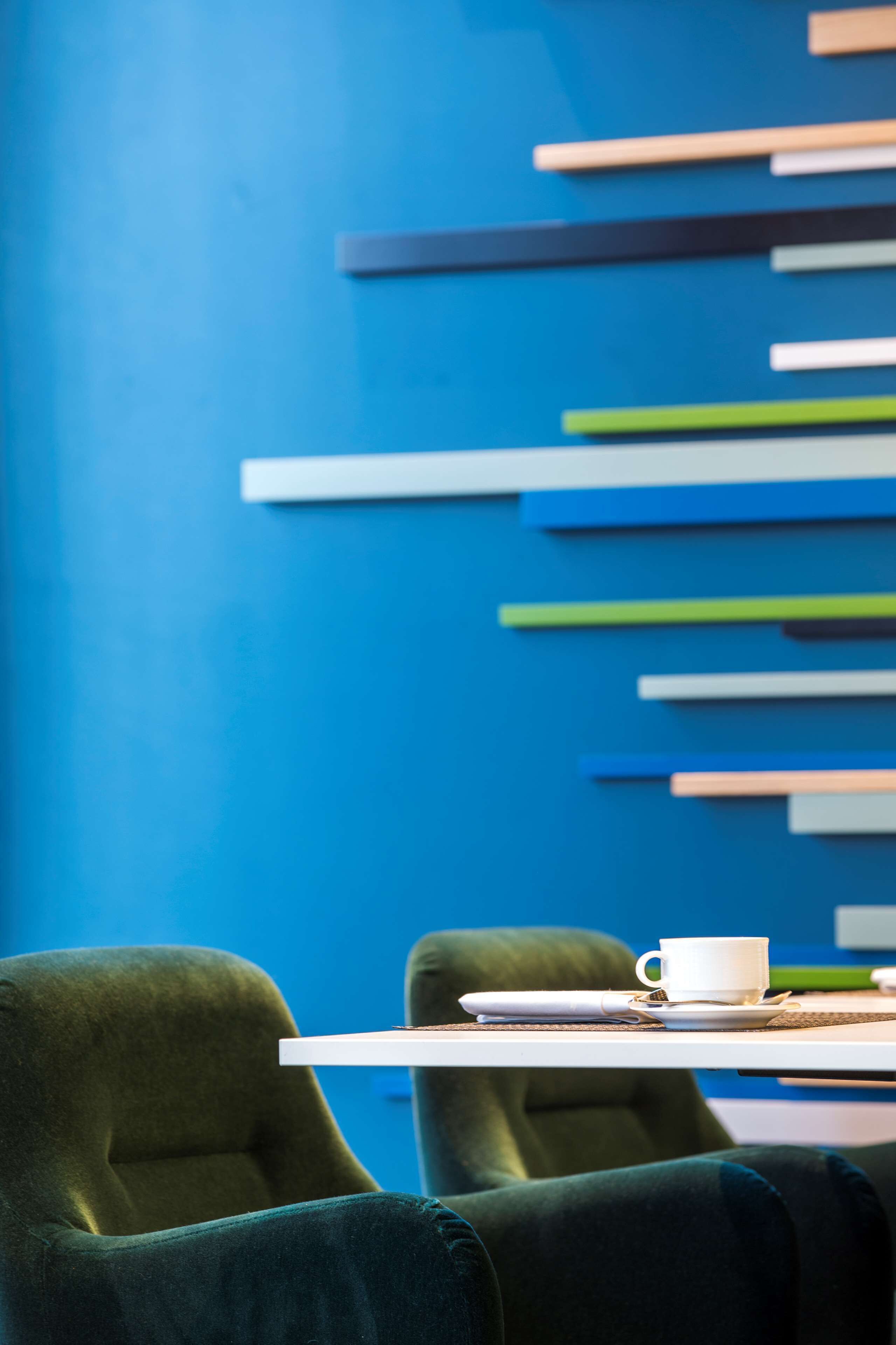 A modern room with a blue wall, a white table, and two green chairs.