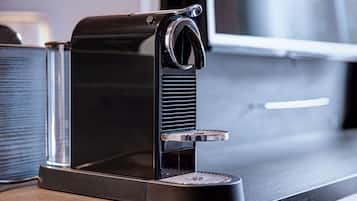 Una máquina de café espresso negra con un depósito de agua transparente y una bandeja metálica para recoger las gotas.