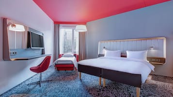 A hotel room with a large bed, a desk with a chair, a TV, and a window with curtains.