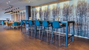 Zona de bar moderna con taburetes azules y una barra larga, con un mural temático de bosque e iluminación empotrada.