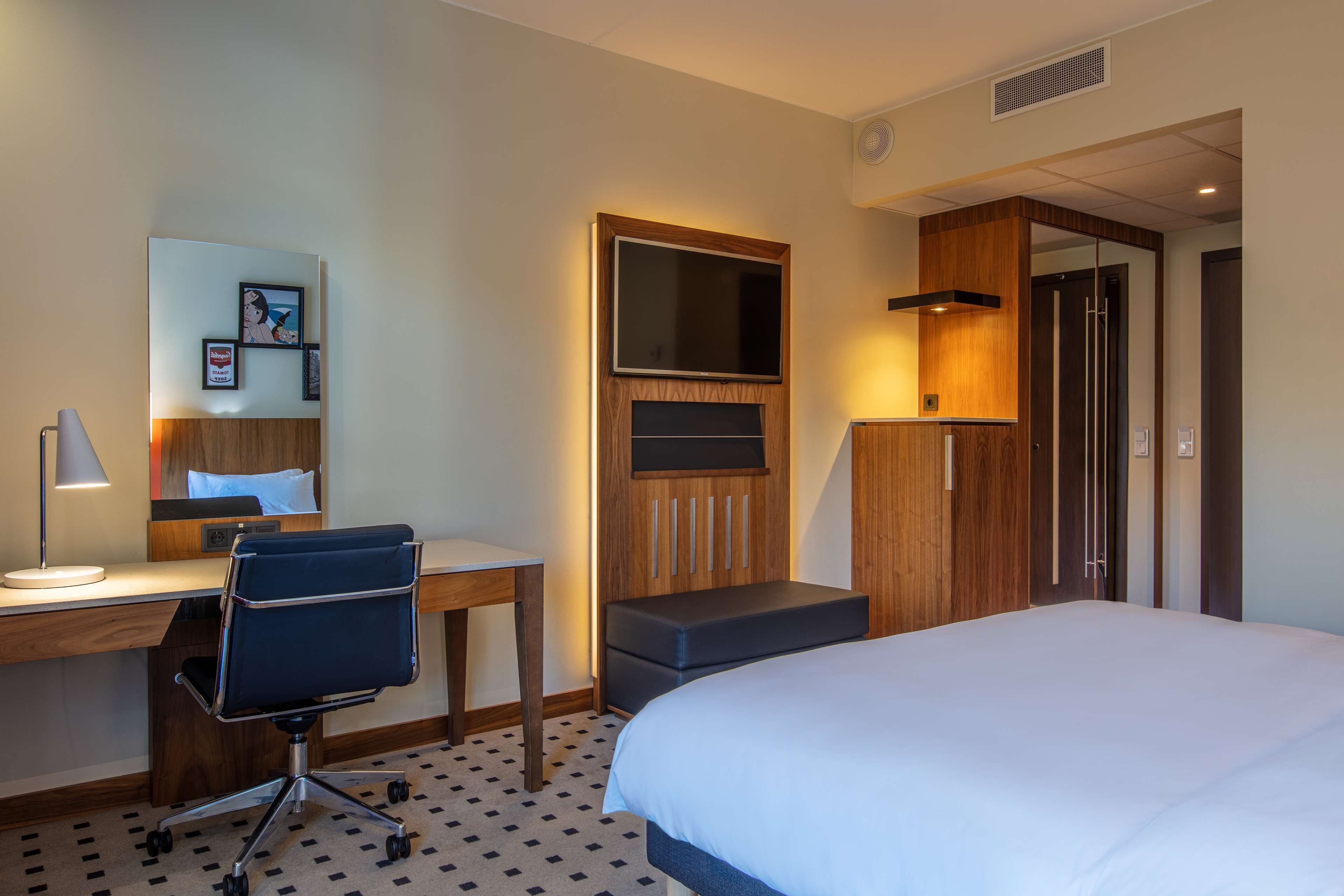 A hotel room with a bed, desk, chair, and a TV mounted on the wall.