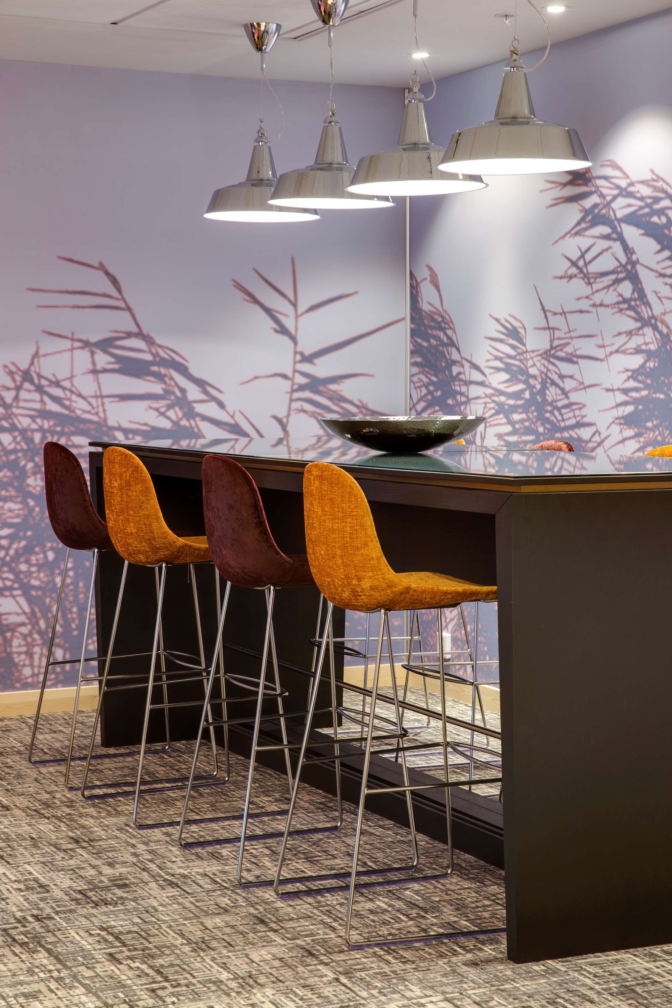 Un espace bar au design moderne, comprenant un comptoir sombre, quatre chaises et trois lampes suspendues.