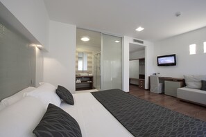 Una habitación de hotel moderna con una cama grande, un escritorio, un televisor y una puerta corredera que da a un baño.