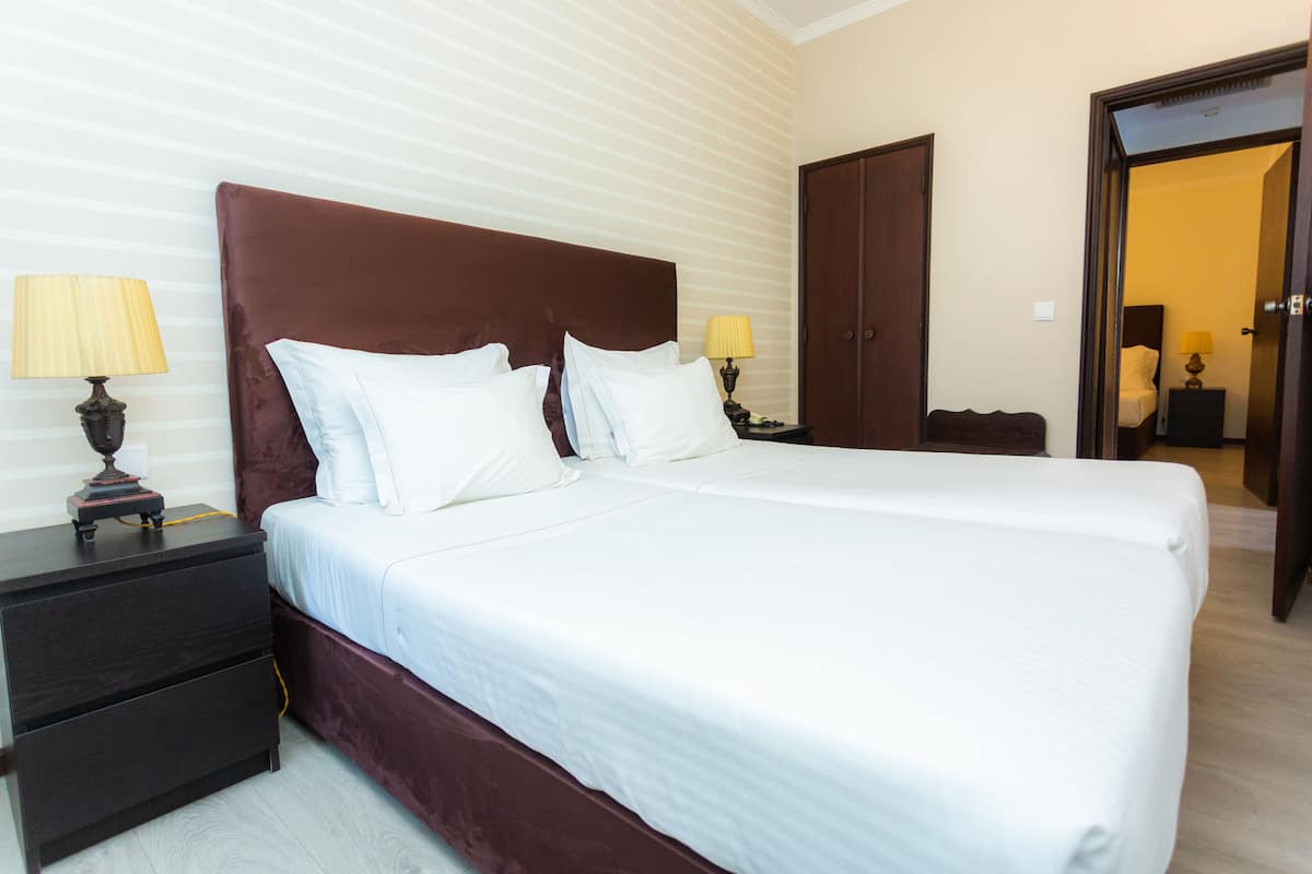 A neatly made bed with white linens and a dark headboard in a hotel room with striped wallpaper and a wooden door.
