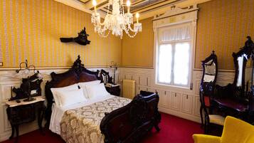 Una habitación con una cama grande, muebles ornamentales, una araña y una ventana con cortinas.