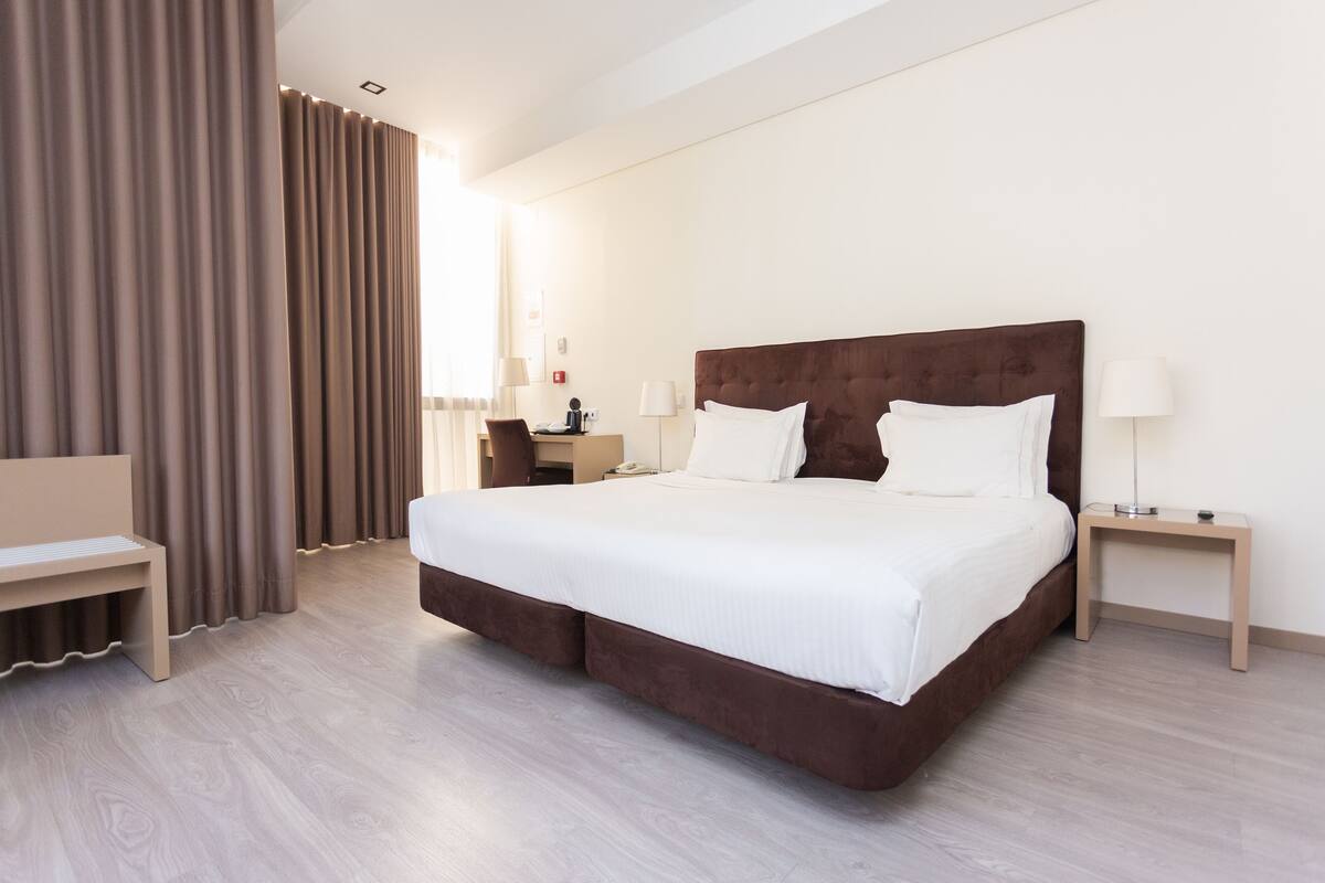 A modern hotel room with a large bed, a desk, and a chair.
