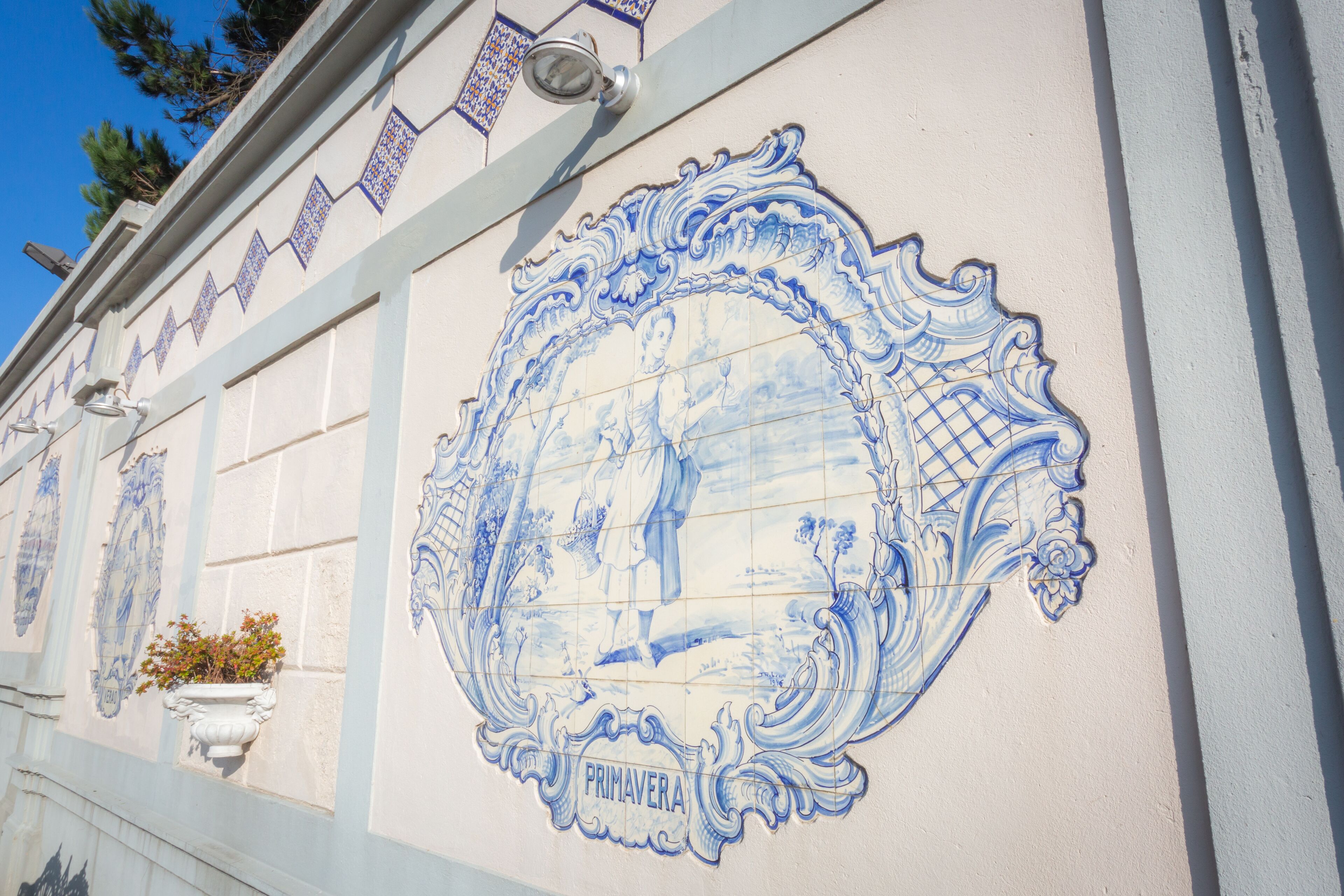Pared con azulejos azules y blancos que muestran una escena detallada y la palabra 'PRIMAVERA'.