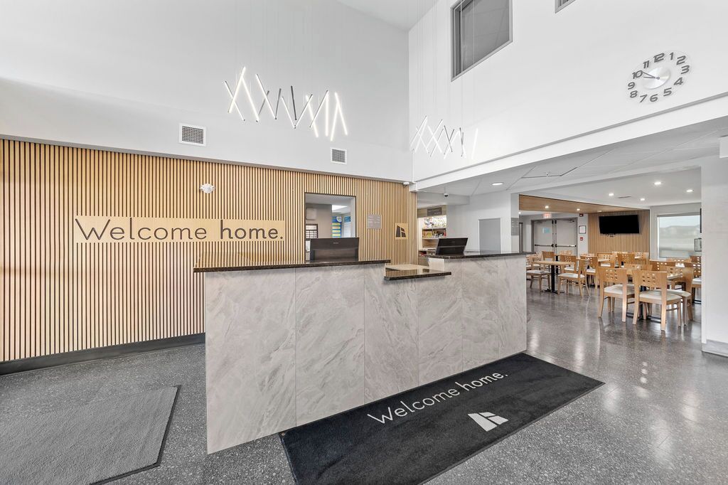 Een modern receptiegebied met een 'Welcome home' bord, een receptiebalie en een zithoek met tafels en stoelen.
