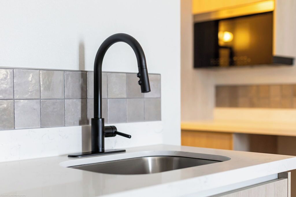 A modern kitchen with a sleek black faucet, a stainless steel sink, and a tiled backsplash.