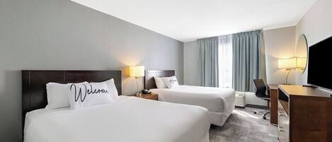 A hotel room with two beds, a desk, a chair, and a TV.
