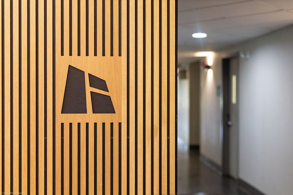 Un panel de madera con un logotipo geométrico, un pasillo con una puerta y una lámpara.