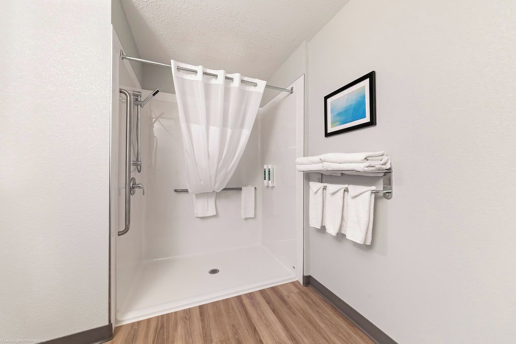 A shower with a white curtain, a towel rack with folded towels, and a framed picture on the wall.