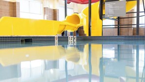 Una piscina con un tobogán amarillo y un cartel que indica las normas del parque acuático.