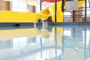 Una piscina con un tobogán amarillo y un cartel que indica las normas del parque acuático.