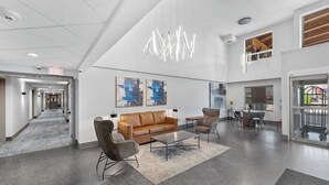 Un vestíbulo amplio con diseño moderno, que incluye un sofá de cuero, sillones, una mesa de centro y arte abstracto en la pared.