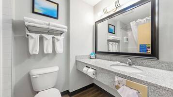 A modern bathroom with a toilet, sink, and large mirror. There are towels hanging on a rack and a framed picture on the wall.