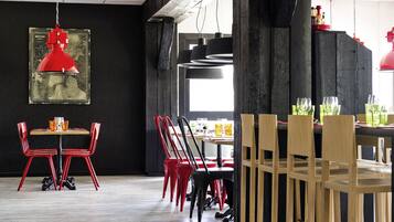 Un comedor con sillas rojas y negras, una mesa de madera y lámparas colgantes rojas.