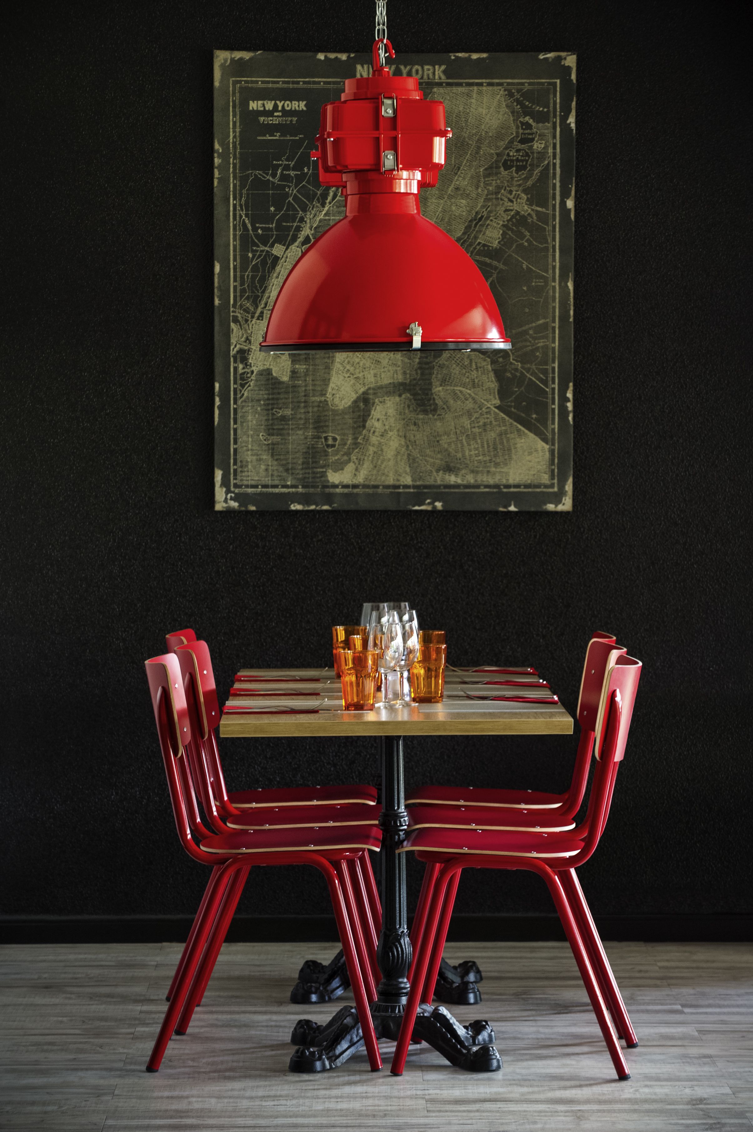 A dining table with red chairs, a red pendant light, and a vintage map on the wall.