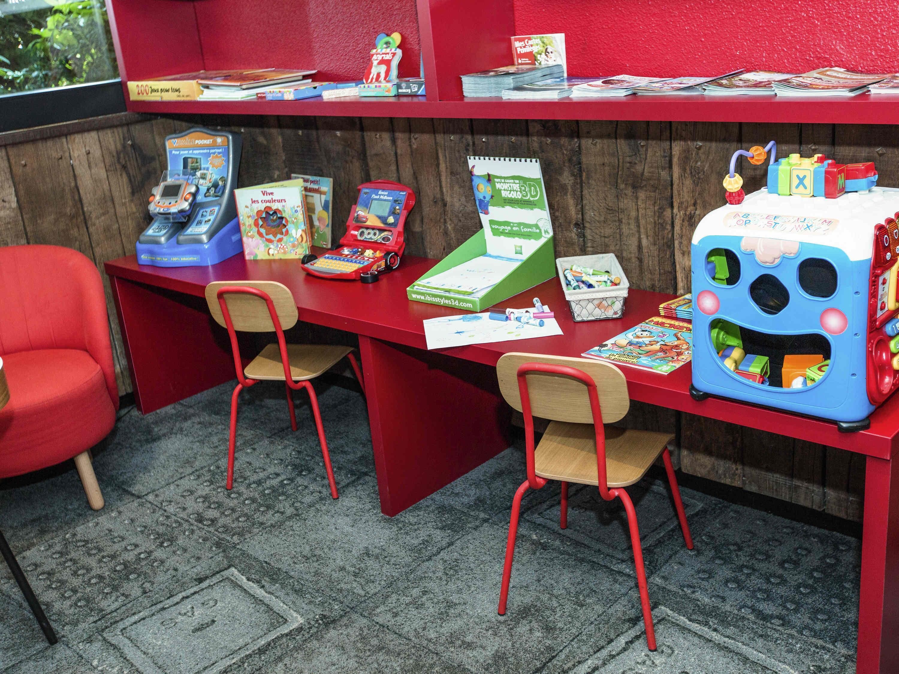 Un área de juegos infantiles con mobiliario rojo, juguetes educativos y libros.