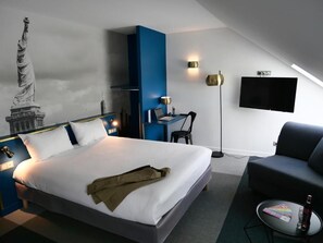 Une chambre d’hôtel avec un lit, un bureau, une chaise, un téléviseur et une statue de la Statue de la Liberté accrochée au mur.