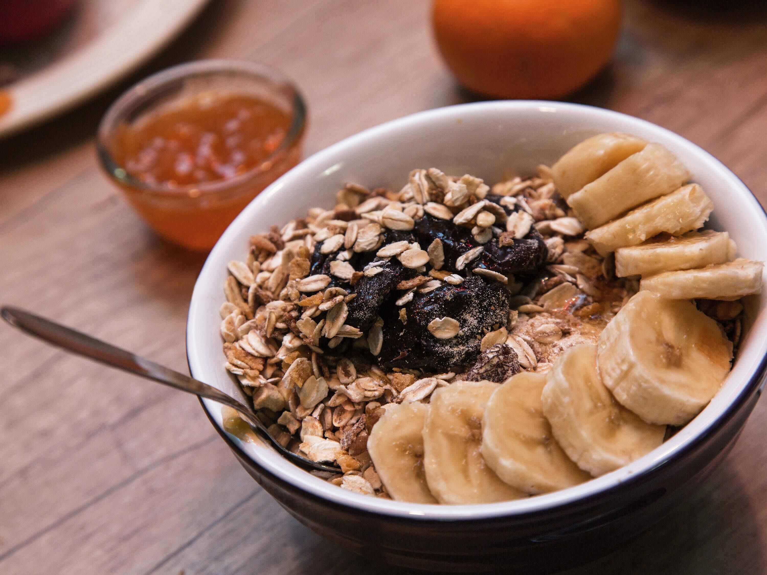 A bowl of cereal with bananas and dried fruit on a wooden table.