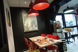 Un coin repas avec une table en bois, des chaises rouges et un mur noir orné d’une carte.