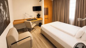 Habitación de hotel con cama, escritorio, silla, televisor y cortinas.