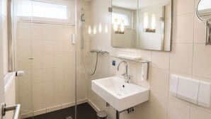 Un baño moderno con cabina de ducha de vidrio, un lavabo blanco y un espejo grande.