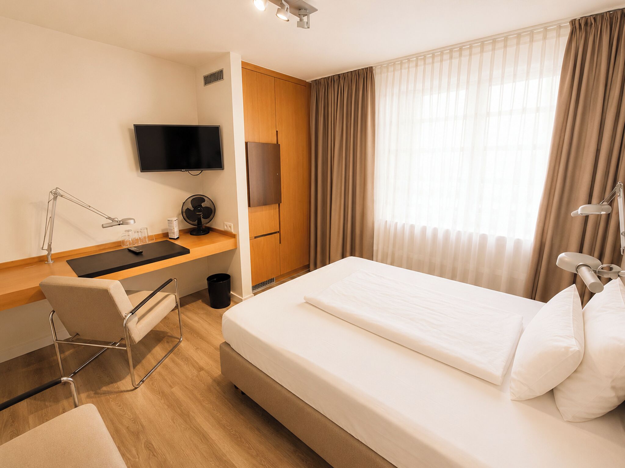 Una habitación de hotel con una cama, un escritorio con una computadora, un televisor y una silla.