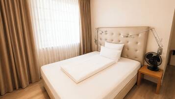 Een hotelkamer met een groot bed, een nachtkastje met een lamp en een raam met gordijnen.