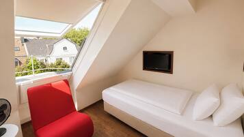 Une petite pièce moderne, avec un fauteuil rouge, un canapé blanc et un téléviseur fixé au mur.