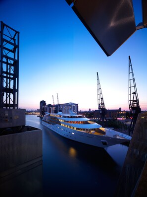 A large, modern cruise ship docked at a port with industrial cranes and buildings in the background. - Sunborn London (London)
