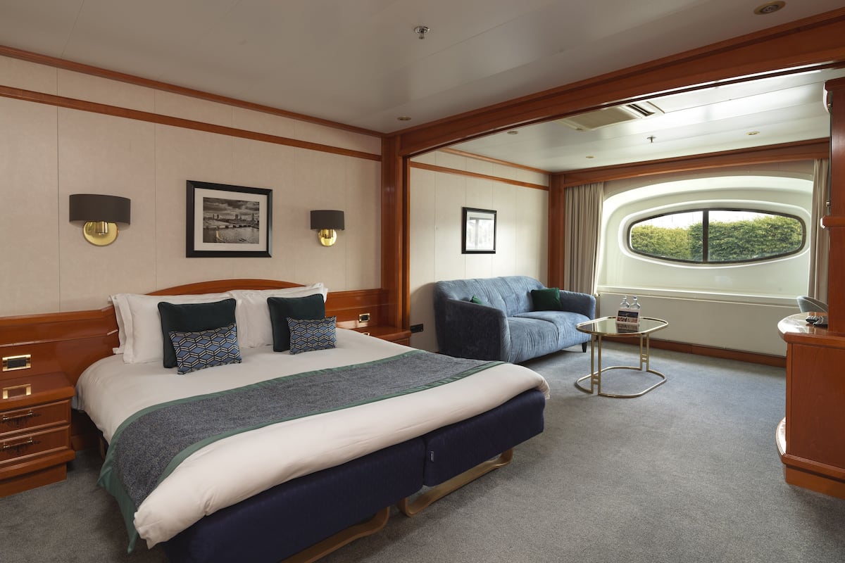 Quarto de hotel com cama grande, sofá, mesa pequena e janela com vista.