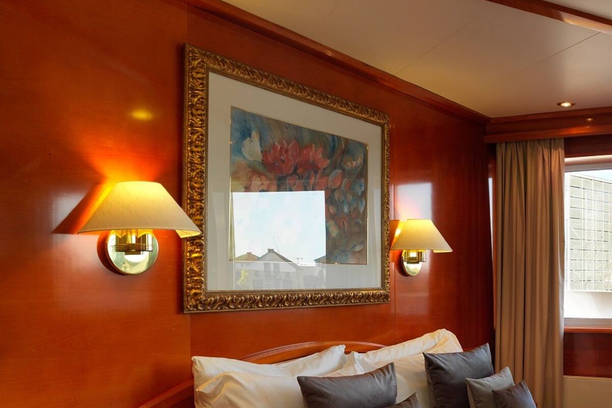 Quarto de hotel com uma cama grande, duas luminárias de cabeceira, uma mesa de cabeceira com um tablet e um quadro emoldurado acima da cama.