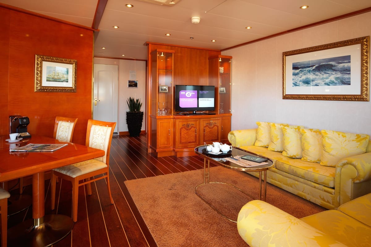 Quarto de hotel com área de refeições, sofá, televisão e uma grande janela.
