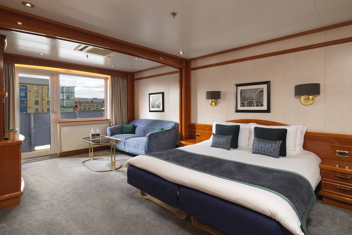 Quarto de hotel com uma cama grande, área de estar com uma poltrona, uma mesinha e vista para edifícios pela janela.