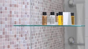 A bathroom with a tiled wall, a glass shelf with toiletries, and a white sink area.