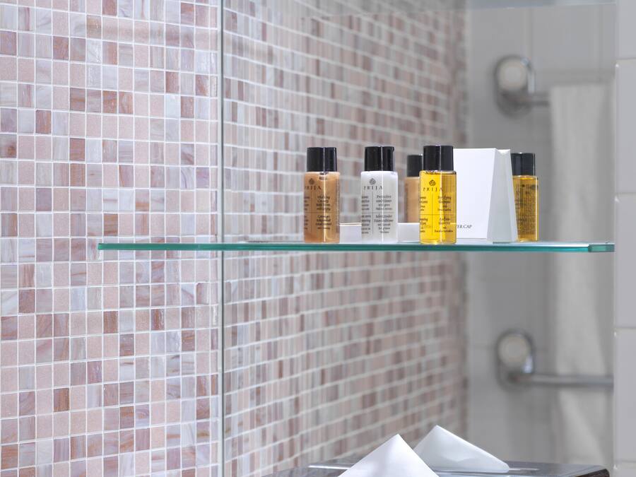 A bathroom with a tiled wall, a glass shelf with toiletries, and a white sink area.