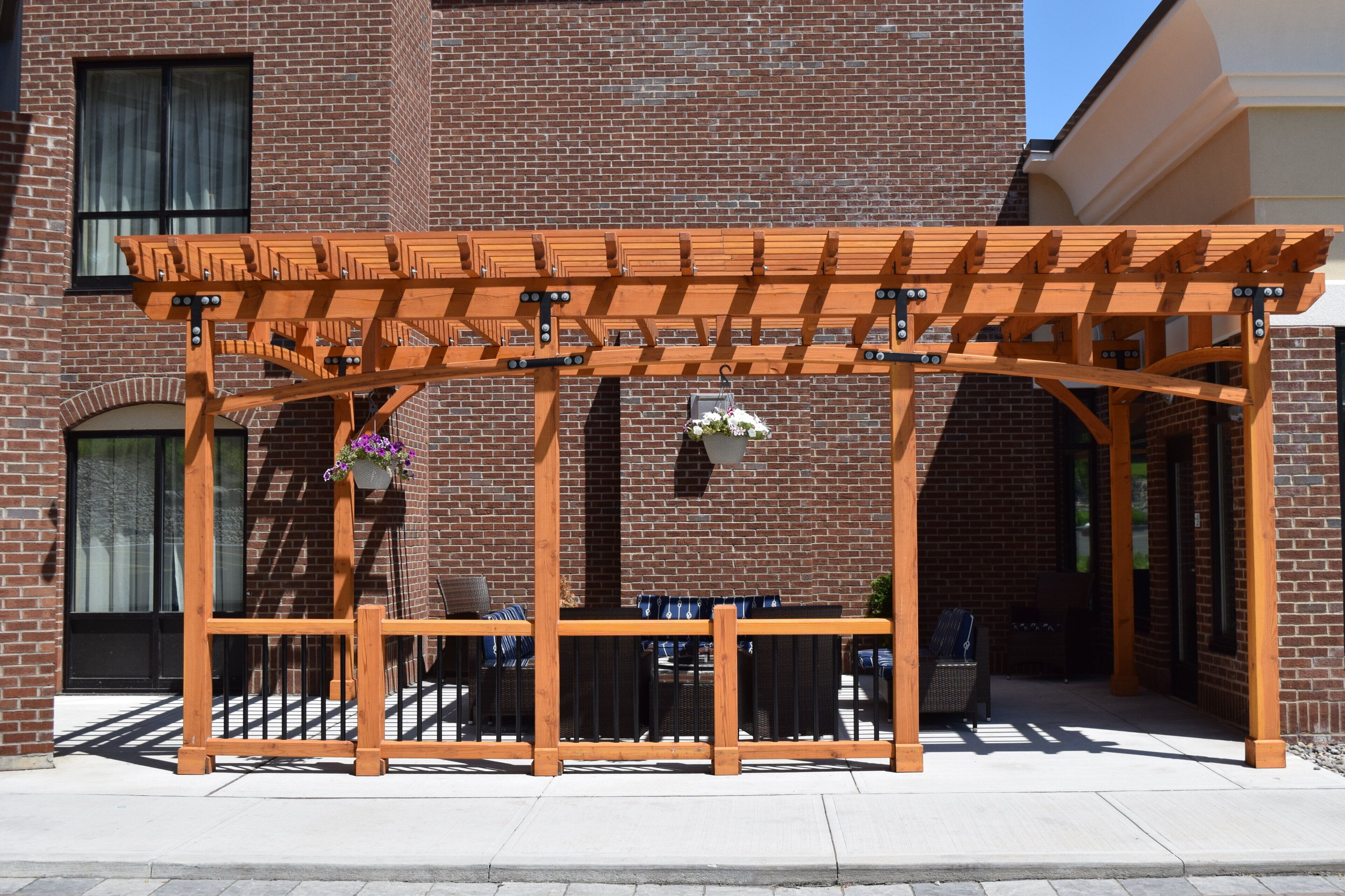 A wooden pergola structure with a brick building in the background.